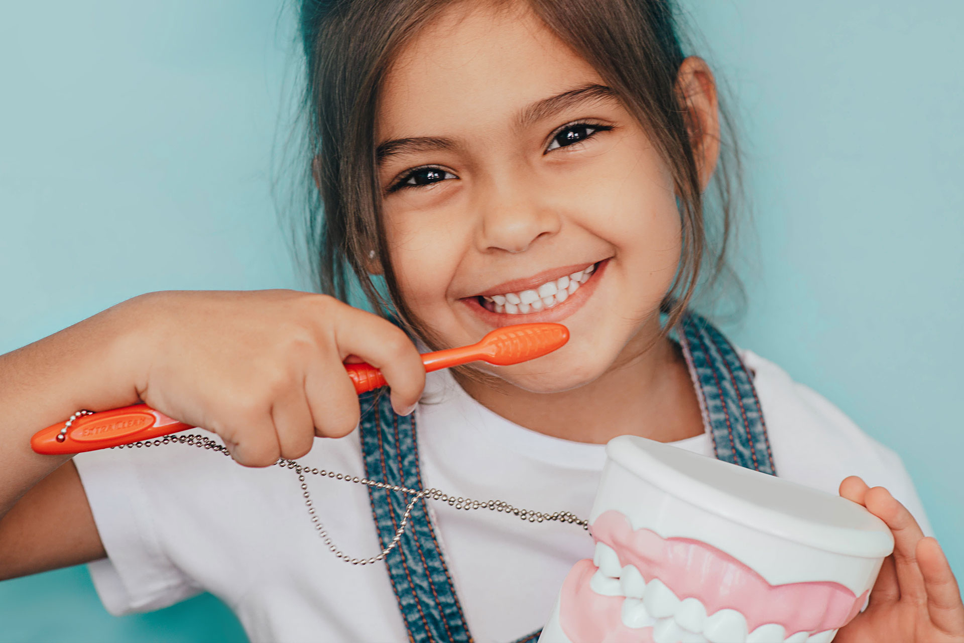 A young girl smiling while holding a pair of red scissors and showing her teeth.