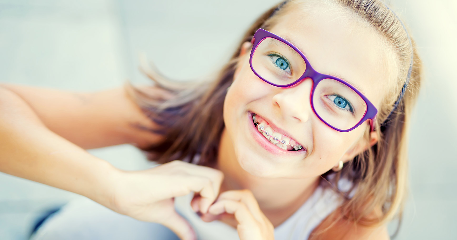 A young girl with glasses and a blue heart in her hand, smiling at the camera.