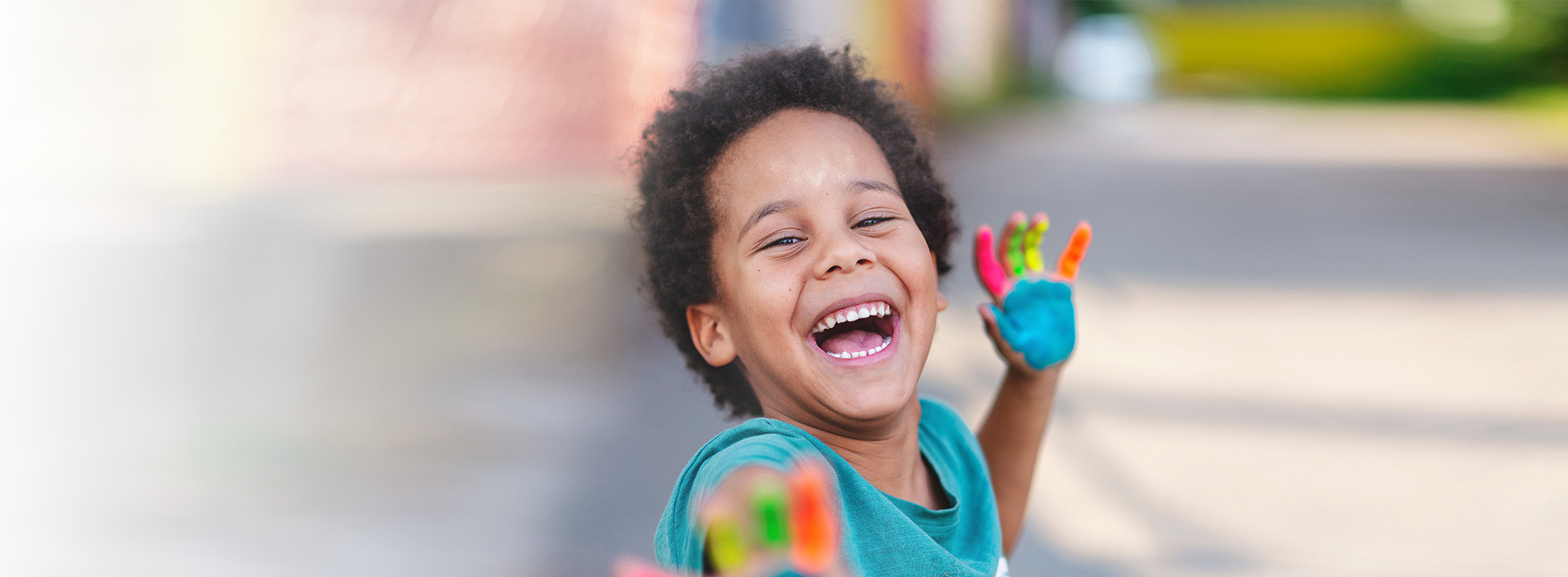 A young child joyfully laughing and holding a colorful object, set against an outdoor backdrop.