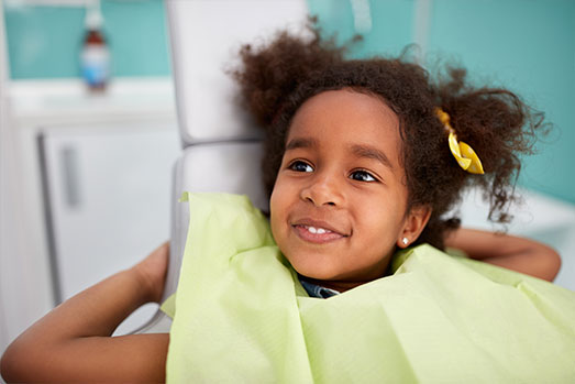 Girl in a dental chair, smiling and looking towards the camera.