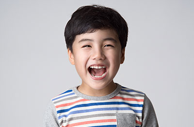 A young boy with a joyful expression, smiling widely, against a neutral background.