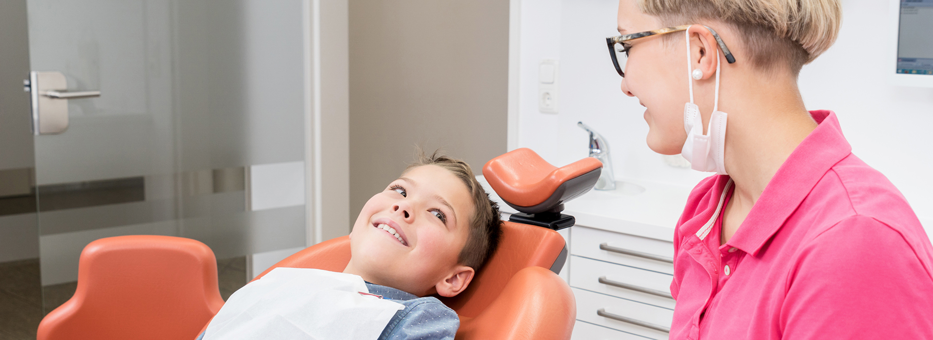 A dental hygiene scene with a child in the chair, a dentist at work, and a parent observing.