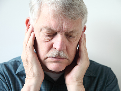 An elderly man with a mustache, holding his head and appearing to be in pain or discomfort.